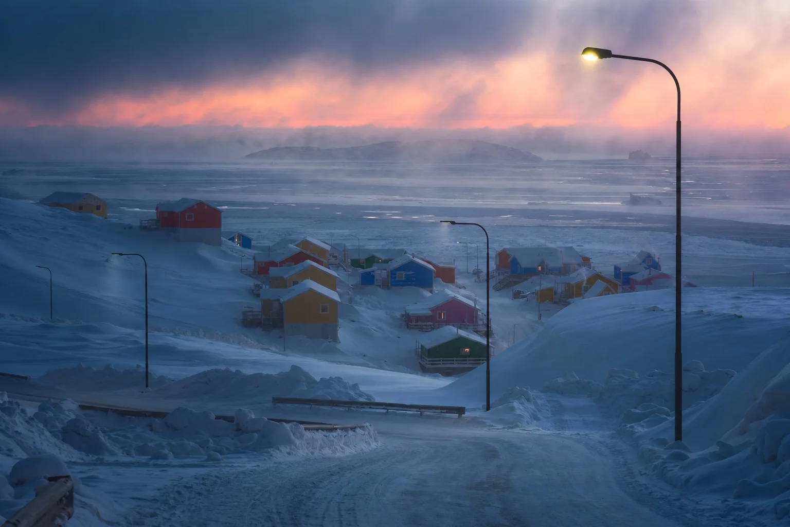 A snow-covered settlement and an empty road at dusk